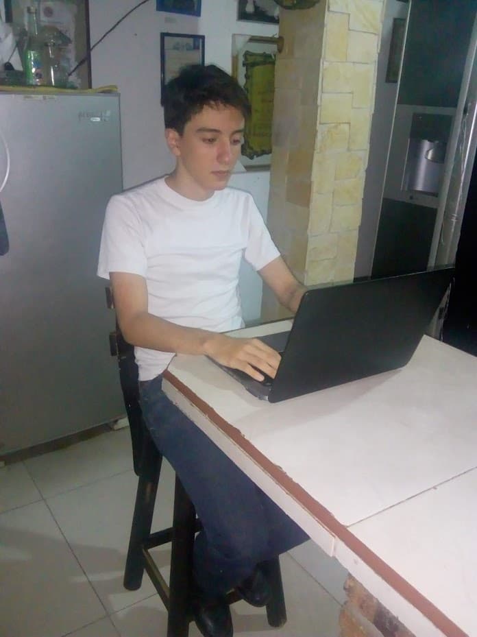 A younger me in a white t-shirt at the kitchen counter, hunched over a laptop, typing.