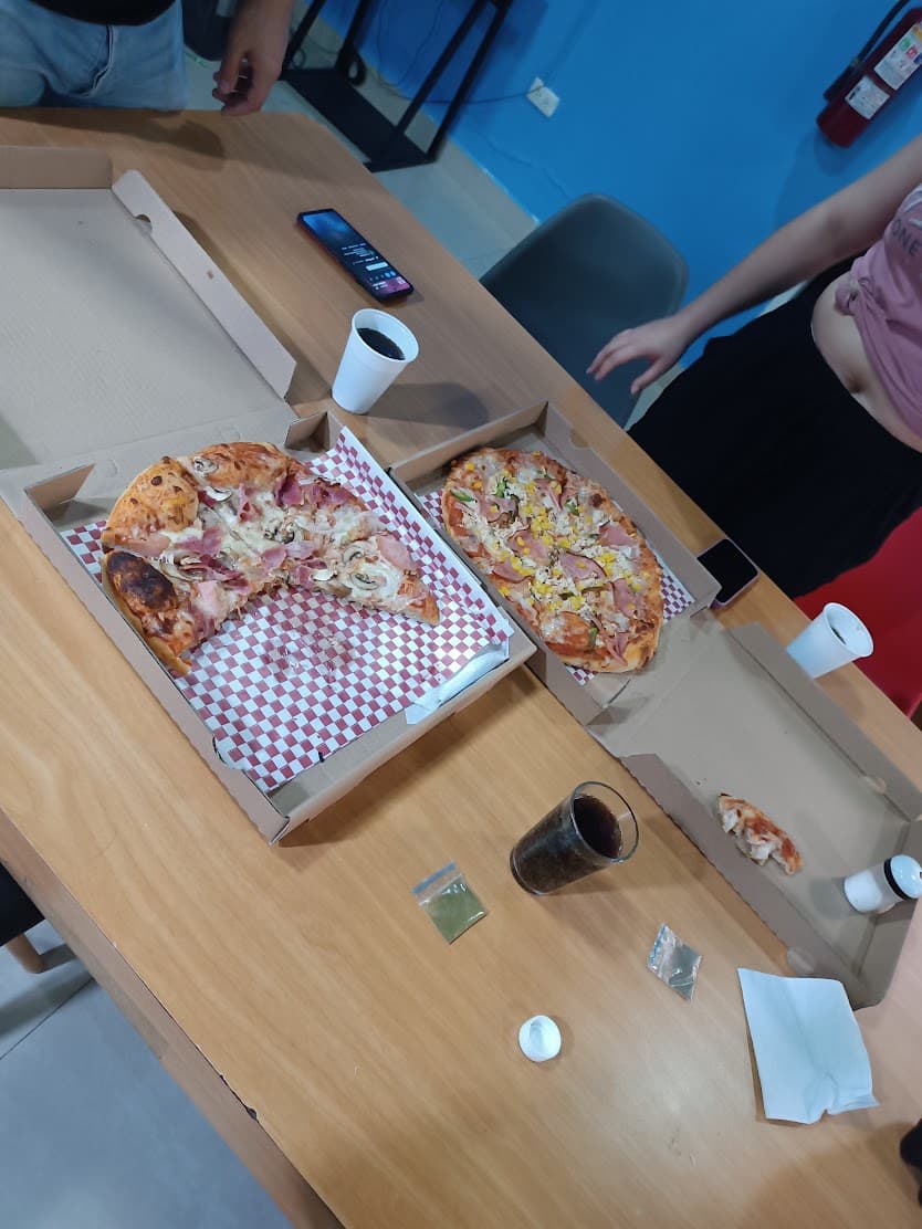 Two open pizza boxes on a meeting-room table, with cups, a phone and the team around it.