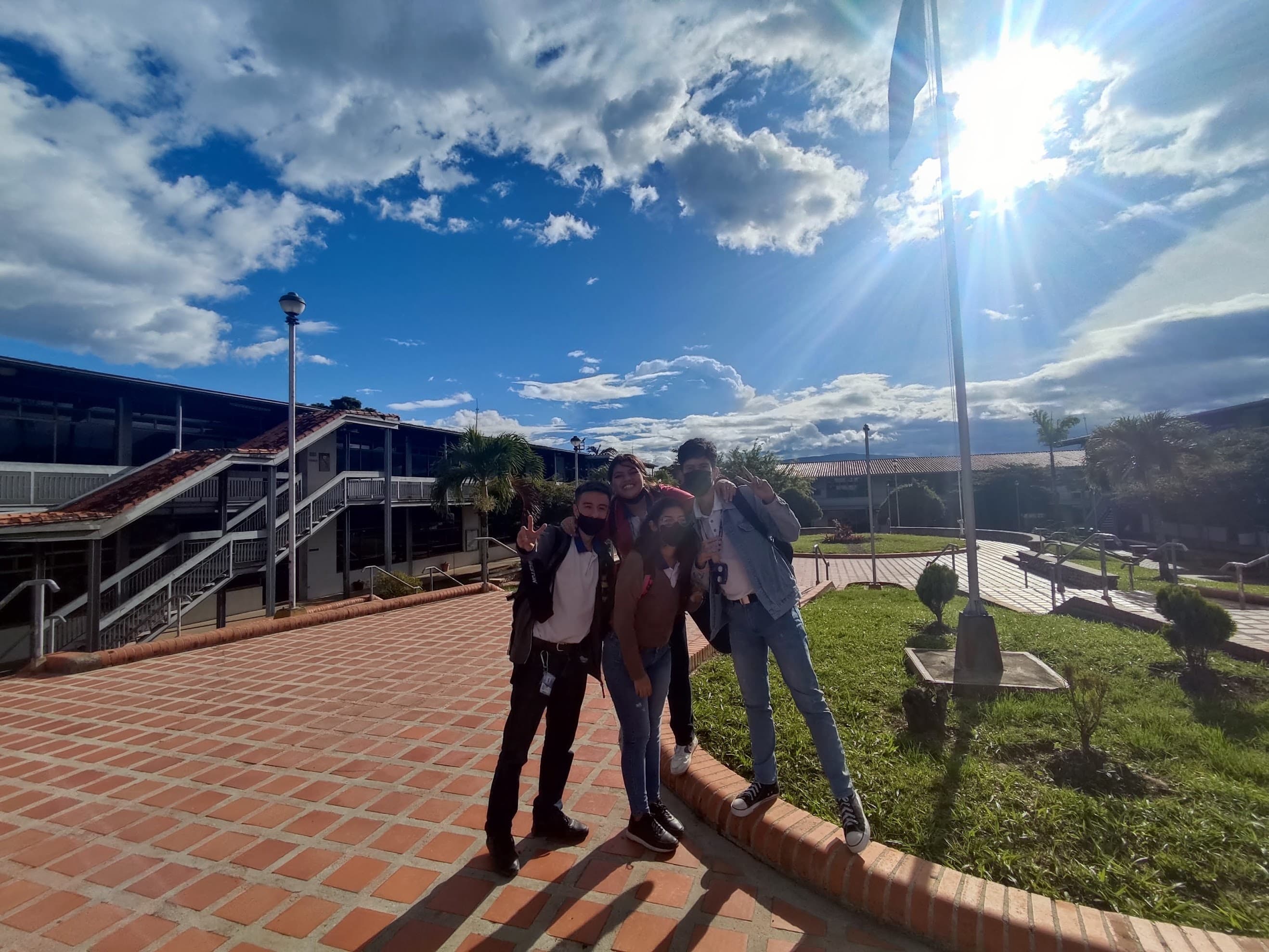 Four of us posing outside the UNEFA campus on a bright day, still in face masks, with the flagpole and the walkways behind.