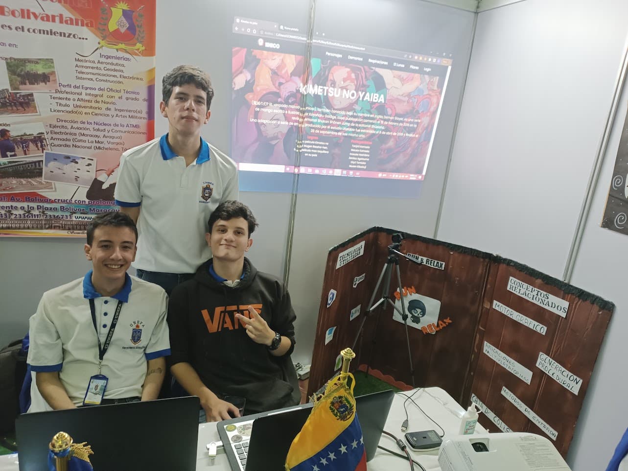 Three of us at a stand at a university fair, with our project on a screen behind and a hand-lettered board listing the technologies we used.